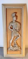 Full view of the vertically oriented framed wall plaque showing the Roman soldier figure standing with one foot raised on a rock base.