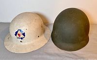 Pair of metal military helmets, one tan with insignia and one olive green plain helmet.