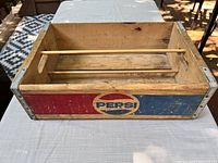 Front side showing the Pepsi logo in faded red, white and blue paint on natural wood with metal corners and two wooden rods inside.