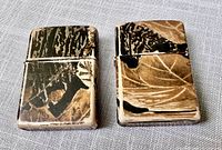Pair of camouflage Zippo lighters side by side showing top and front surfaces
