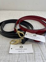 Two patent leather pet leashes, one red and one black, coiled and displayed with Hartman & Rose brand tags attached.