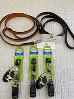 Two patent leather pet leashes in orange and black coiled on a light cloth background with three green-packaged Forever Pals dog collars in camouflage pattern below.