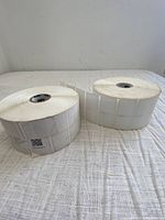 Two large rolls of white rectangular peel and stick labels on a fabric surface.