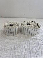 Two rolls of white peel and stick label tape with black vertical lines on a white fabric surface.