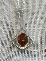 Front view of sterling silver pendant with an oval amber stone set in a diamond-shaped silver frame on a silver chain.