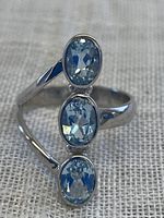 Front view of the sterling silver ring showing three vertically aligned faceted blue topaz gemstones on a textured fabric background.