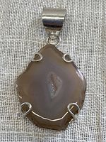 Close-up photo of banded agate geode slice pendant showing natural banding, polished surface, and silver plated prong setting.