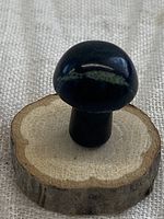 Side angle showing the smooth polished oval mushroom shape with rounded cap and narrow stem, placed on a natural wood slice base to highlight the stone's shape and color.