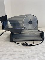 Full side view of the slicer showing blade, food guard, and base with power cord wrapped at front.