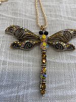 Front view of the gold-tone dragonfly pendant with faceted clear, gold, black, and iridescent rhinestones.