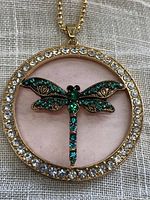 Front view of gold tone dragonfly pendant with green and clear faceted rhinestones on a gold tone chain.