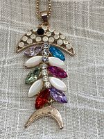 Front side of the fish pendant necklace showing multicoloured faceted rhinestones on gold tone metal.