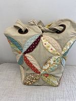 Full view of the beige fabric bag with colorful quilted petal patchwork on front