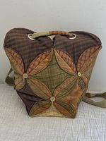 Front view of the hand quilted backpack showing patchwork quilt in brown, tan, green, and orange plaids with button details.