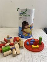 Overview of the set with loose wooden blocks of multiple shapes and colors, round red base with block cutouts, and the cylindrical container.
