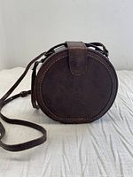 Front view of round brown leather purse with strap closure and visible stitching