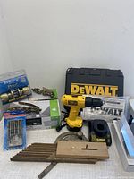 Full lot overview showing DeWalt drill in case, light box, lock set, screwdriver set, metal chains, wooden base tool, charger and shower head.