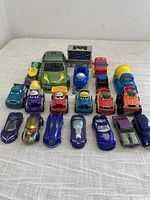 Photo of 21 assorted toy cars and trucks, various colors and styles on white fabric surface