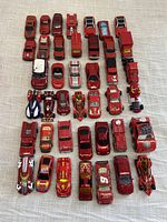 Top-down view of 41 red diecast toy cars arranged in rows on fabric surface showing various car types and brands.