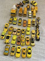 Top view of 39 yellow toy vehicles arranged in rows including various cars, trucks, motorcycles, and a helicopter. Mostly metal construction, used condition.