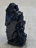 Close-up front view of a shiny black rough shungite chunk showing natural jagged shapes and reflective surfaces.