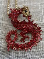 Front view of dragon pendant necklace showing detailed red faceted rhinestones and gold tone finish with rhinestone eyes.