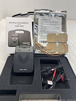 TENS 3000 device, instruction manual, electrode pads, user guide, and cables arranged in foam-padded carrying case.