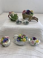 Full group of seven porcelain floral pieces including two swan figurines, floral basket, teapot, and other floral decor pieces