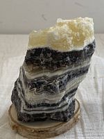 Front view of Zebra Calcite mineral specimen showing black and white banding with pale yellow crystalline top on wooden base
