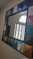 Full view of the decorative wall mirror showing the colorful raised square panel frame and beveled mirror center.