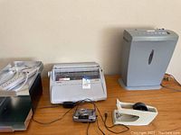 Photo showing Brother GX-6750 electronic typewriter, paper shredder, Canon Z115 camera, tape dispenser on wooden table.