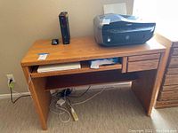 Full view of wooden computer desk with keyboard tray, one drawer, and contents on top including printer, modem/router, mouse, and laptop on keyboard tray. Shows the desk's overall structure and size.
