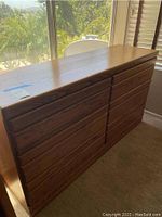 Wooden six-drawer dresser with natural finish seen from an angle in a bright room near window.