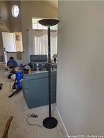 Full view of black metal floor lamp standing next to a wall with a baseboard and visible cord on the floor.