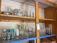 Shelf display of assorted glassware, showing various clear and blue glass items including tumblers, bowls, and stemmed glasses.