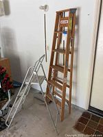 Full view of both ladders side by side: metal step ladder with shiny aluminum frame and wooden ladder leaning against wall