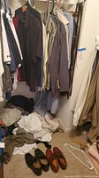 Photo showing men's large shirts hanging on a rack along with several pairs of pants and shoes on the floor