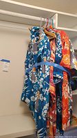 Photo showing multiple men's Hawaiian shirts hanging on a closet rod, including blue and red floral prints.