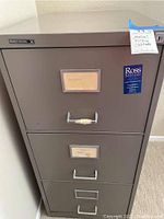 Front view of the gray metal filing cabinet showing three drawers and a label on top drawer.