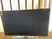 Front view of the Panasonic flat-screen TV showing the black screen and bezel with some reflections and a power cord hanging.