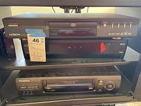 Photo showing the Hitachi DVD/CD player stacked on top of Panasonic VCR, both black, with visible labeled buttons and markings.