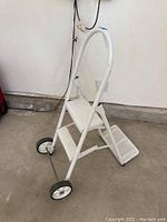 White metal step ladder with two steps and two wheels, angled view showing structure and handle