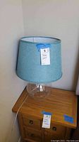 Full view of the table lamp showing blue fabric shade and clear glass base on wooden surface.