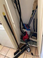 Photo showing collection of cleaning tools including Hoover vacuum, Dirt Devil Can Vac, brooms, dustpan, mop bucket.