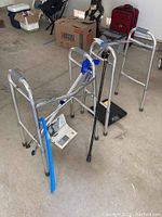 Photo of two aluminum walking frames, black Healthometer scale, blue grabbing stick, and digital blood pressure monitor on a garage floor.