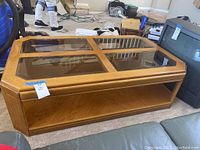 Photo of the rectangular wood and glass coffee table with four glass panels on top and a lower wood shelf. Shows scratches and surrounding environment.