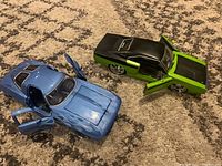 Green and black Charger and baby blue Corvette model cars on carpet, both with open doors showing details.