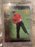 Front of 2001 Tiger Woods Tiger's Tales rookie card in protective plastic case showing Tiger Woods swinging, gold trim, serial numbered 36/100