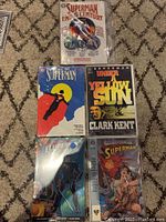 Photo of 5 Superman graphic novels, 4 paperback and 1 hardcover featuring colorful front covers with Superman and related characters.