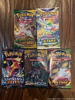 Five sealed Pokemon booster packs from different sets placed on a wooden surface.